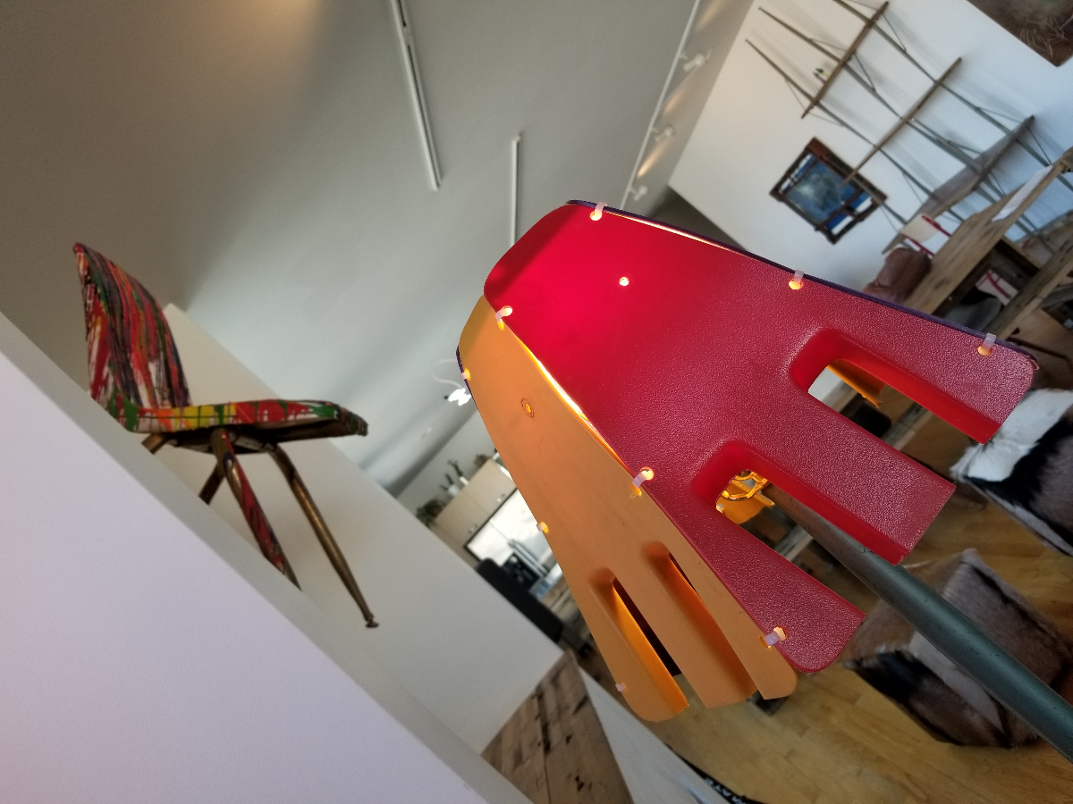 Foreground: The backs of discarded Chicago Public Schools chairs serve as lampshades at an exhibit organized by John Preus and featuring material from closed schools. Background: crayons melted onto a chair from a closed CPS school drip onto the hearth below. (Linda Lutton/WBEZ)