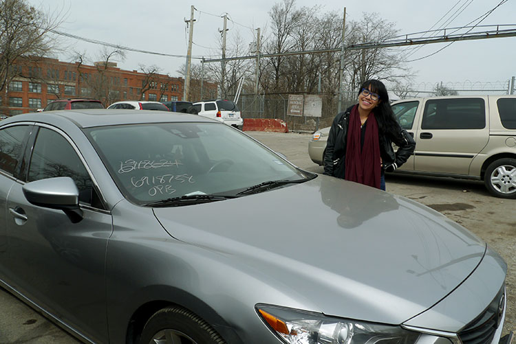 (Elliott Ramos/WBEZ) Alma Acosta, 23, stands with her vehicle at the city's West Side impound lot after it got towed for violating the Chicago's winter parking ban last month.